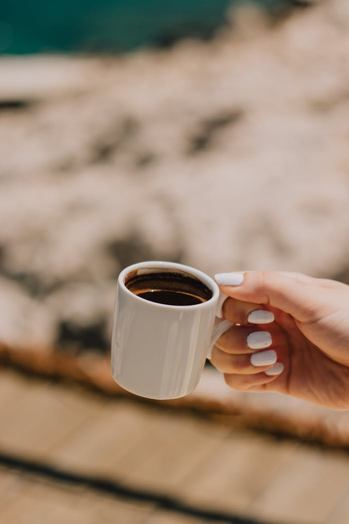 A close-up view of a hand holding a coffee cup with blurred outdoor background.