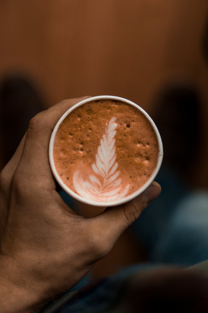 Close-up of latte art in a cup held by a person, showcasing intricate foam design.